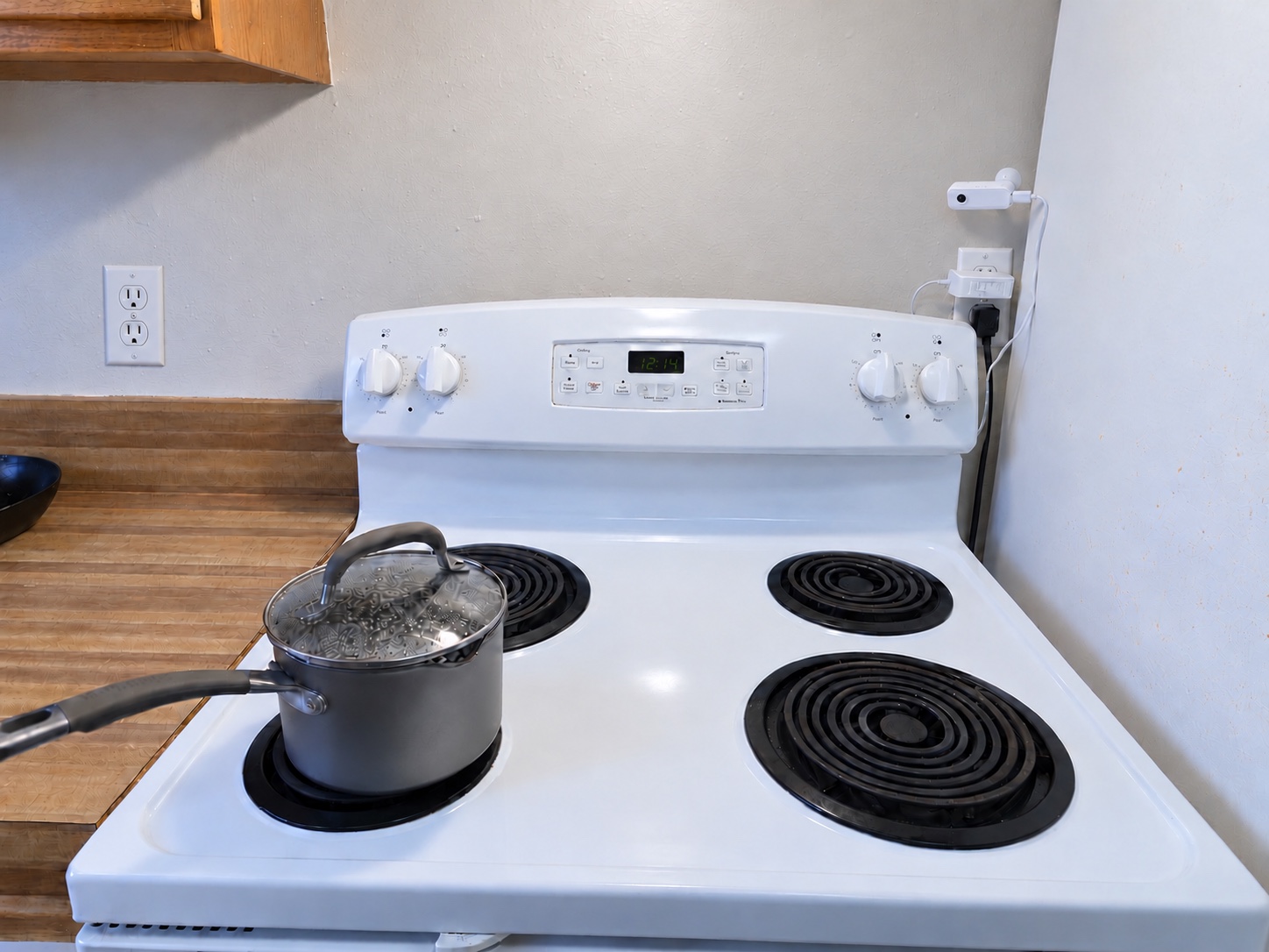 One StoveDetector unit mounted on the backsplash beside an electric stove, with its power cord to the nearby outlet.