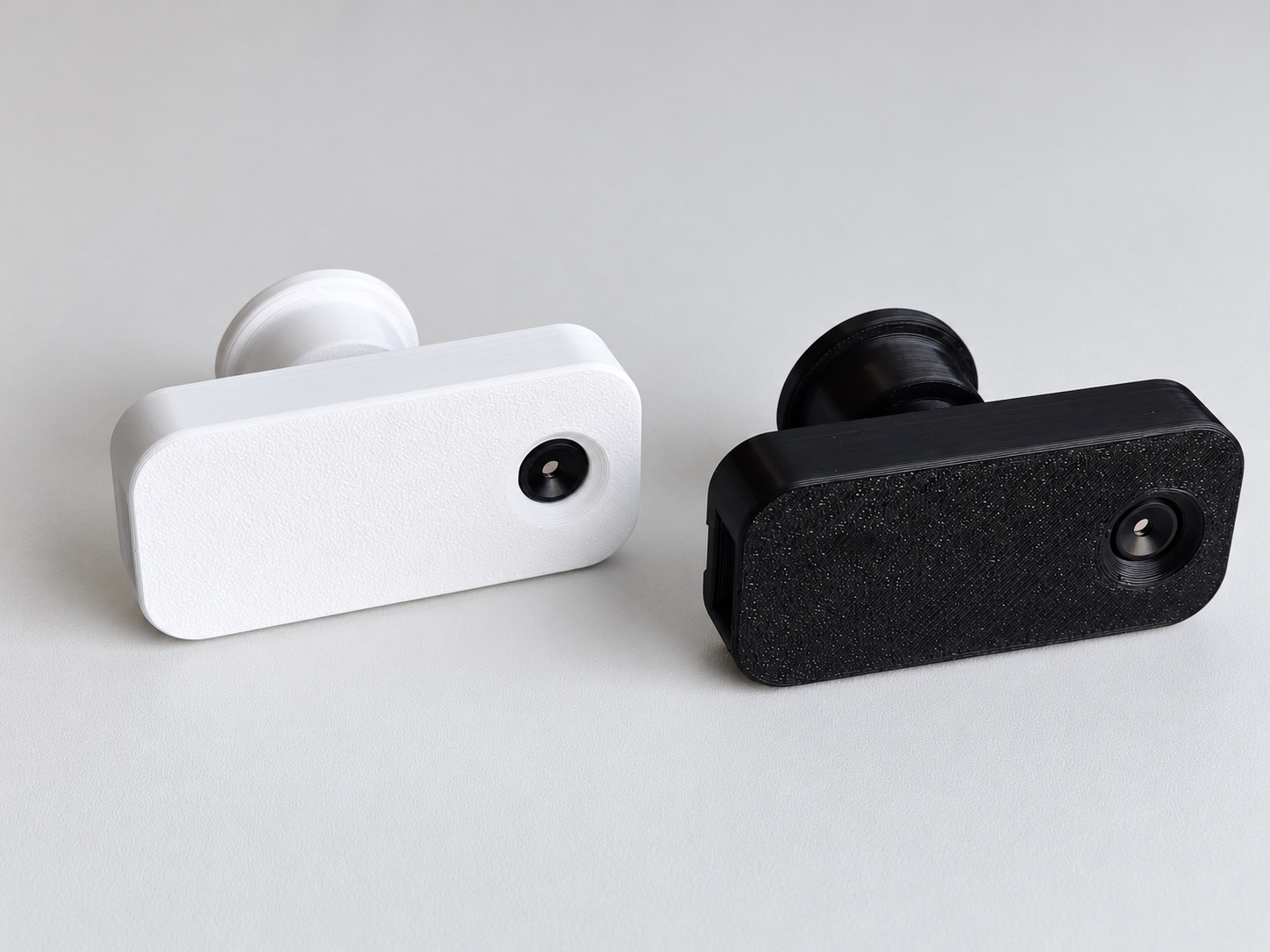 White and black StoveDetector units side by side, showing their textured cases and round heat-sensor windows.